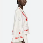 Woman wearing a white outfit with red floral embroidery on a white background
