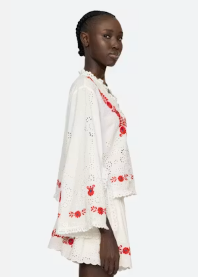 Woman wearing a white outfit with red floral embroidery on a white background