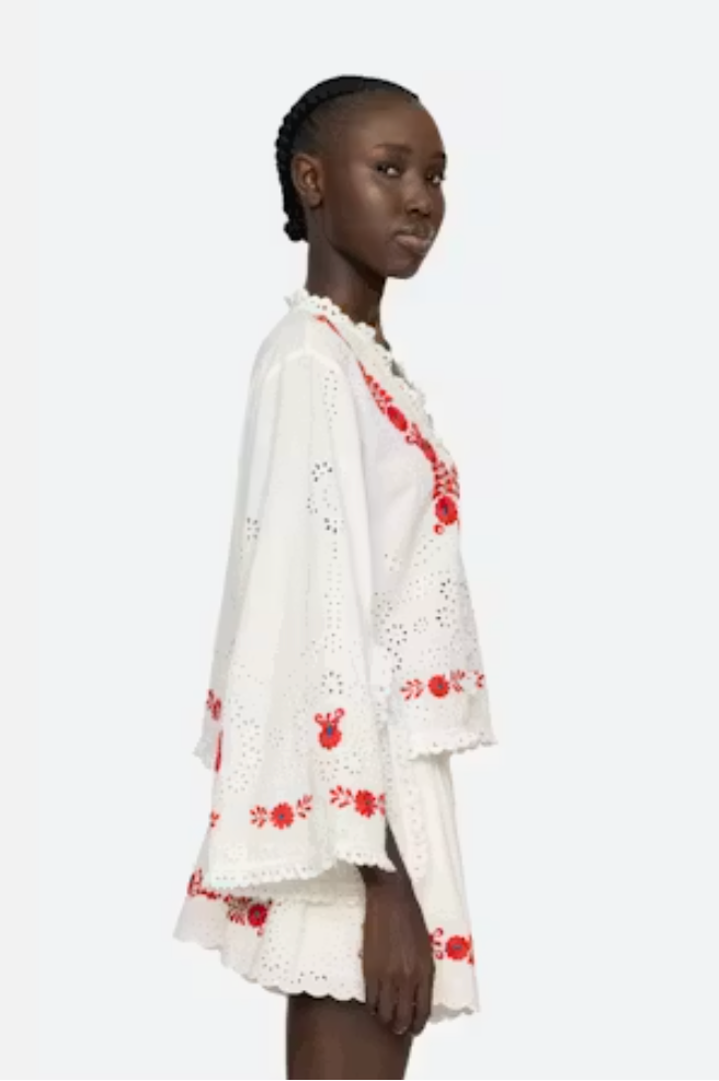Woman wearing a white outfit with red floral embroidery on a white background