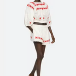 Model wearing a white outfit with red embroidery on a white background