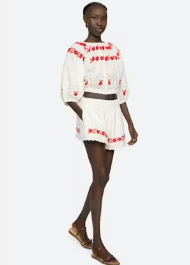 Model wearing a white outfit with red embroidery on a white background