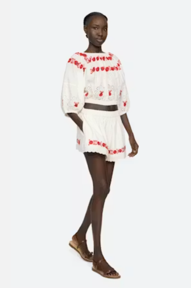 Model wearing a white outfit with red embroidery on a white background