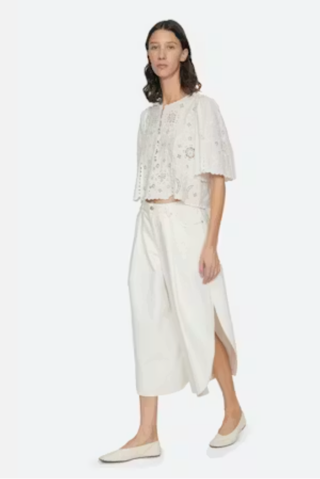 Woman wearing a white outfit with a floral top and wide-leg pants on a white background