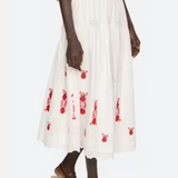 Person wearing a white dress with red floral patterns and brown sandals on a white background
