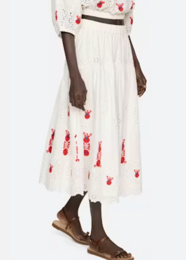 Person wearing a white dress with red floral patterns and brown sandals on a white background