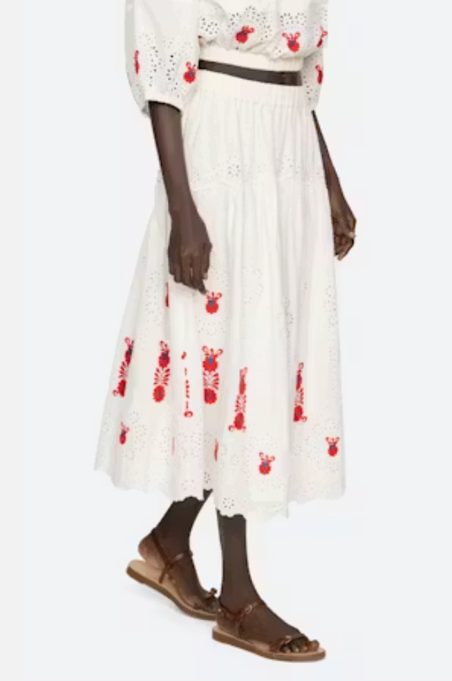 Person wearing a white dress with red floral patterns and brown sandals on a white background