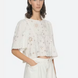 Woman wearing a white embroidered top and pants on a white background