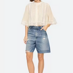 Woman wearing a beige blouse and denim shorts on a white background