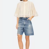 Woman wearing a beige blouse and denim shorts on a white background