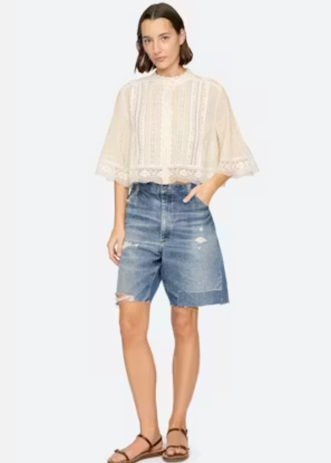 Woman wearing a beige blouse and denim shorts on a white background