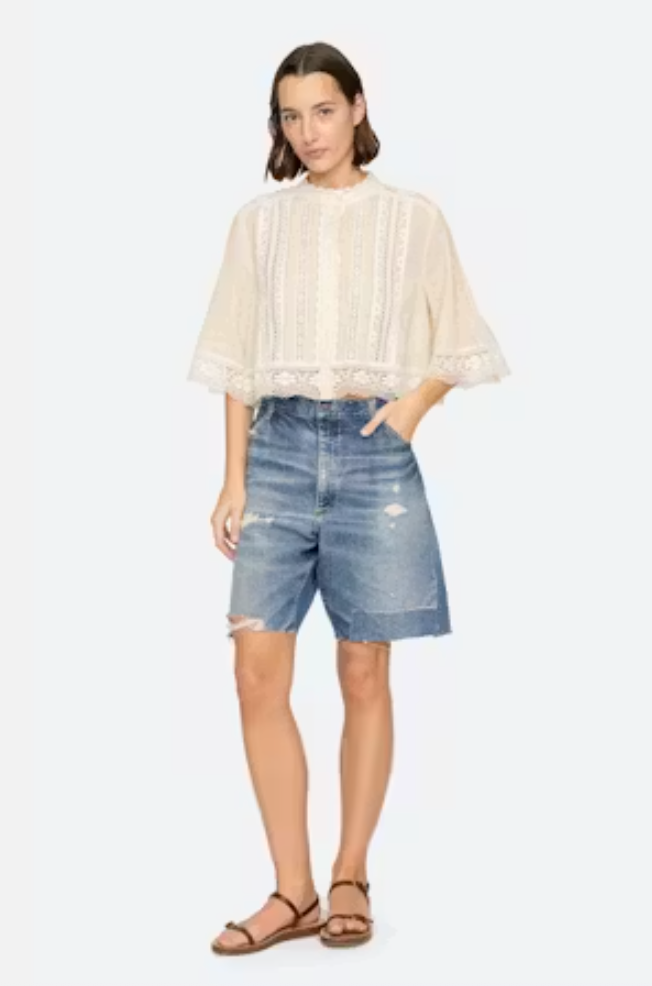 Woman wearing a beige blouse and denim shorts on a white background