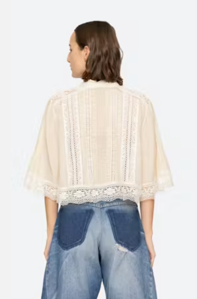 Woman wearing a beige lace top and blue jeans on a white background