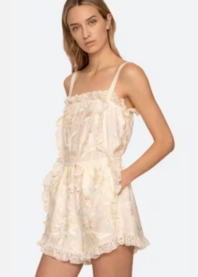 Woman wearing a white lace romper on a plain background