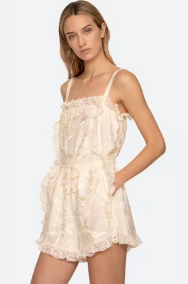 Woman wearing a white lace romper on a plain background