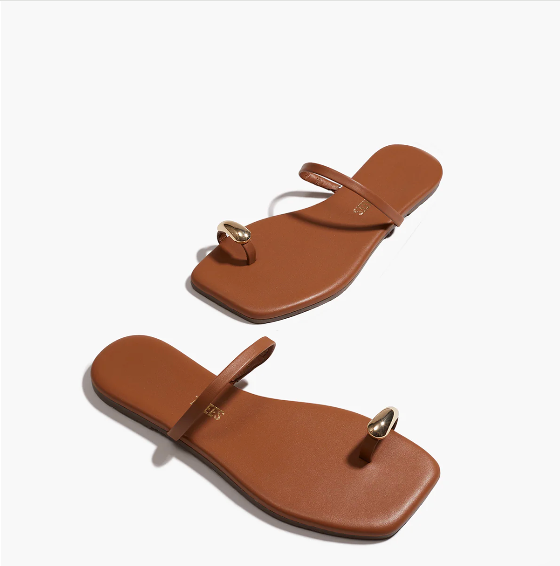 Pair of brown sandals with a gold toe ring on a white background