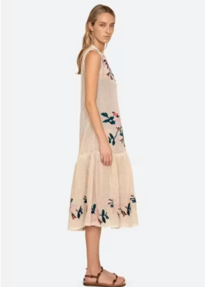 Woman wearing a beige sleeveless dress with floral patterns on a white background