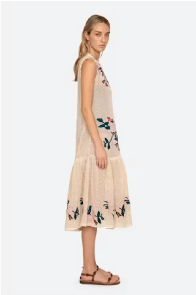 Woman wearing a beige sleeveless dress with floral patterns on a white background