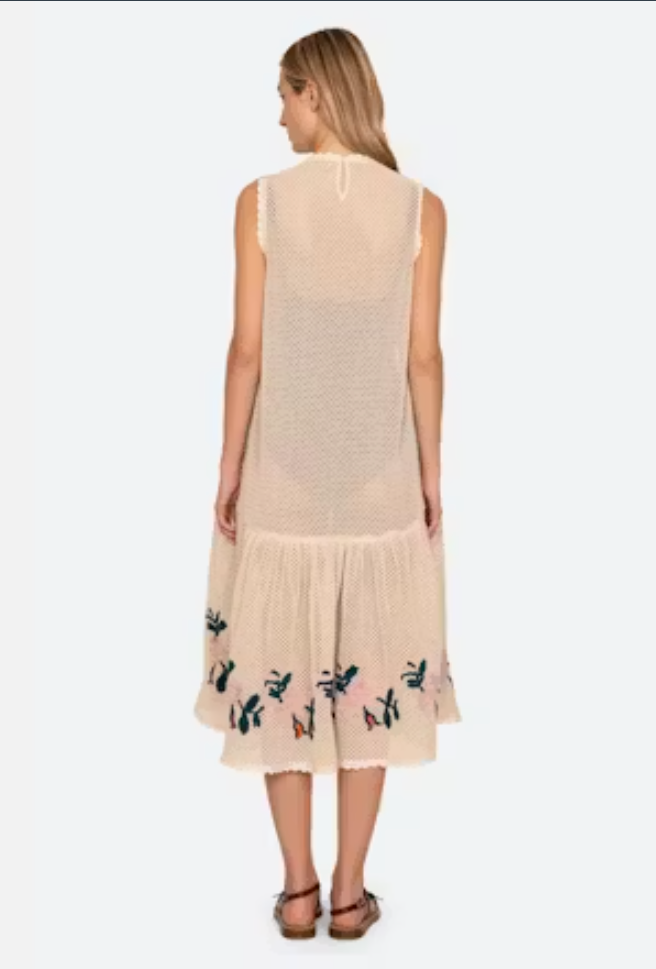 Woman wearing a beige sleeveless dress with floral embroidery on a white background