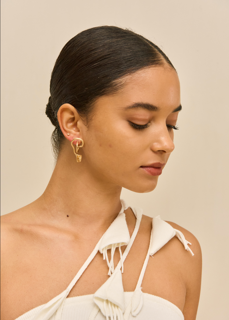 Woman wearing gold earrings with a beige background