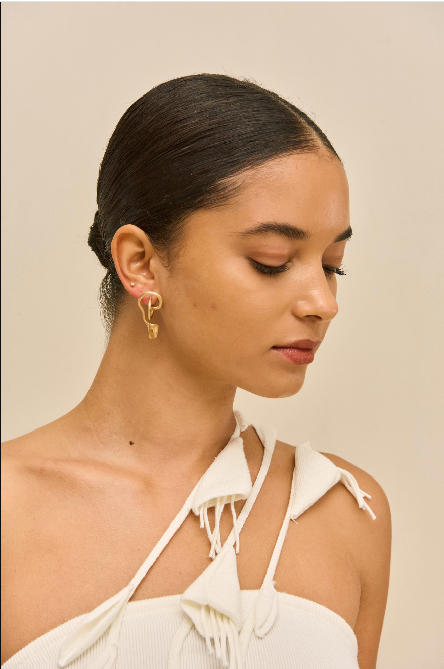 Woman wearing gold earrings with a beige background