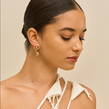 Woman wearing gold earrings with a beige background
