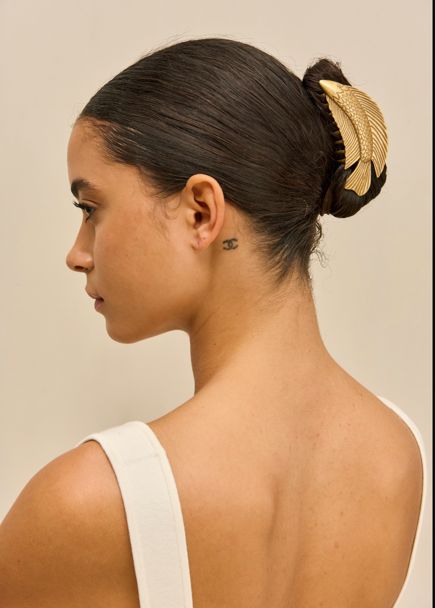 Woman with a stylish hair bun featuring a gold fish hair clip against a neutral background