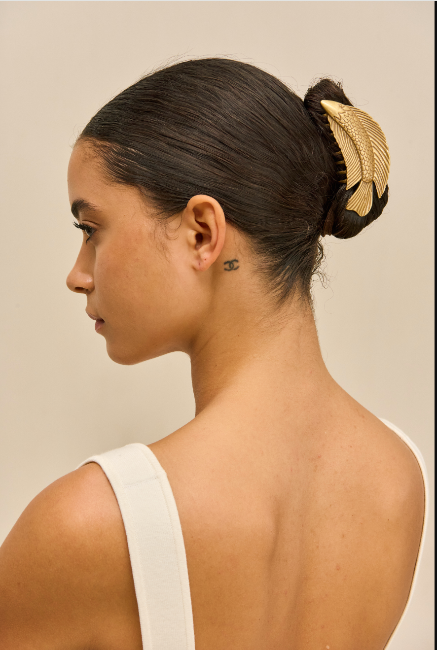 Woman with a stylish hair bun featuring a gold fish hair clip against a neutral background