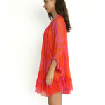 Woman wearing a vibrant orange and pink tie-dye dress on a white background