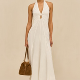 Woman wearing a white halter neck dress holding a brown handbag on a beige background