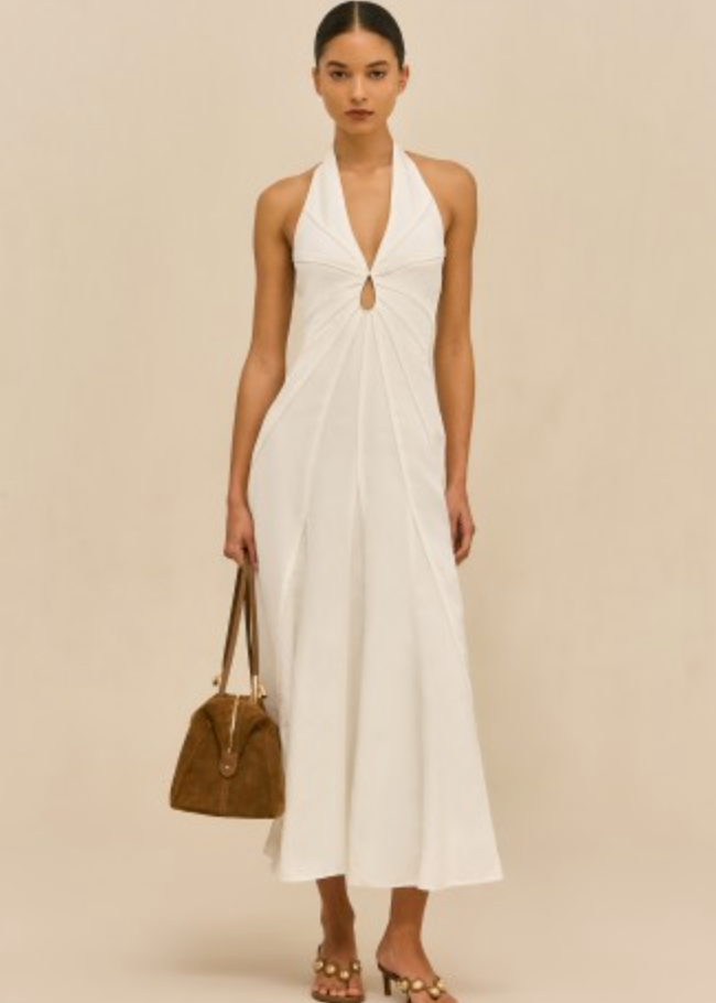 Woman wearing a white halter neck dress holding a brown handbag on a beige background