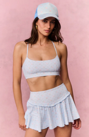 Woman wearing a light blue sports bra and skirt set with a matching cap on a pink background
