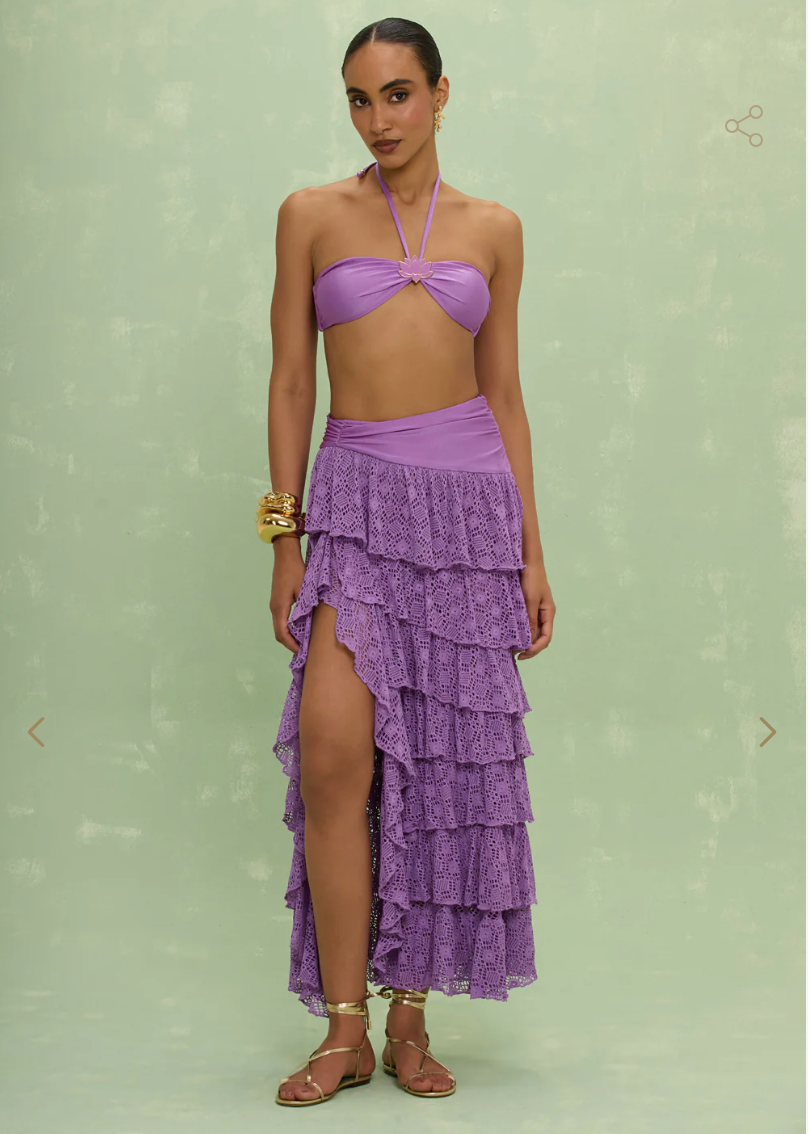Woman wearing a purple tiered skirt over a purple bikini against a light green background