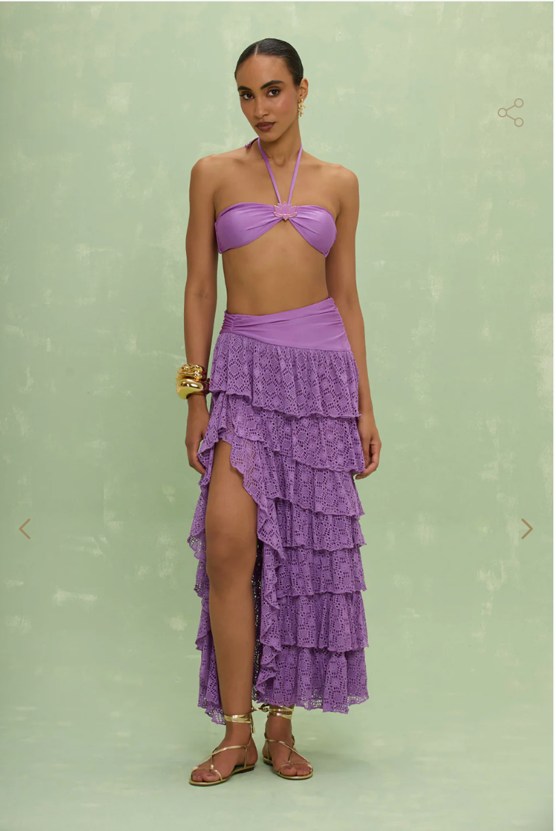 Woman wearing a purple tiered skirt over a purple bikini against a light green background