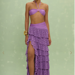 Woman wearing a purple tiered skirt over a purple bikini against a light green background