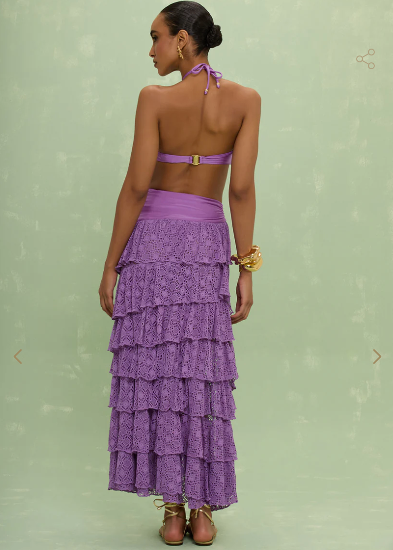 Woman wearing a purple tiered skirt over a purple bathing suit against a light green background