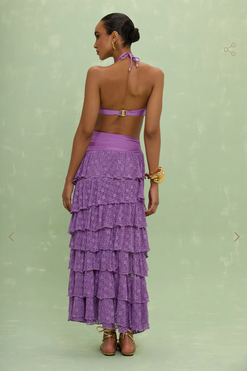 Woman wearing a purple tiered skirt over a purple bathing suit against a light green background