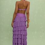 Woman wearing a purple tiered skirt over a purple bathing suit against a light green background