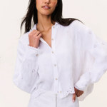 Woman wearing a white blouse with intricate detailing on a plain background