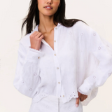 Woman wearing a white blouse with intricate detailing on a plain background
