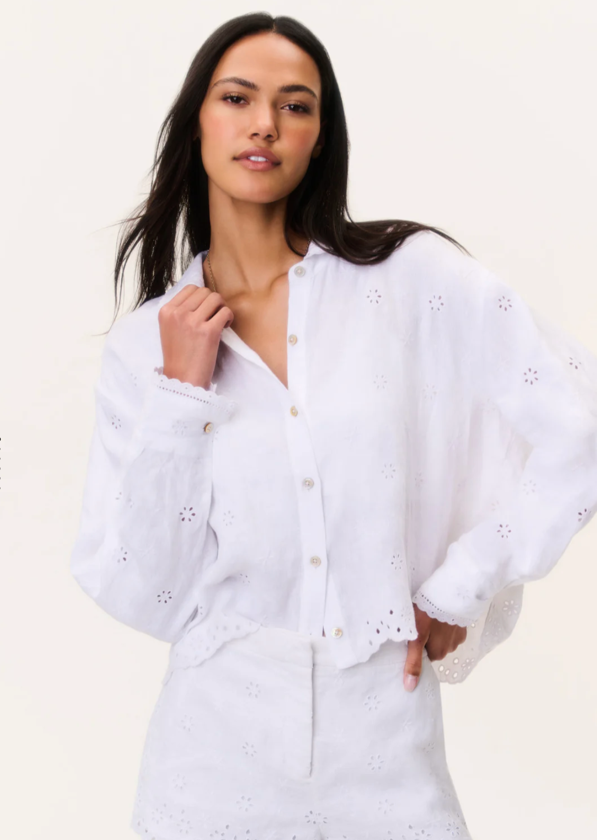 Woman wearing a white blouse with intricate detailing on a plain background