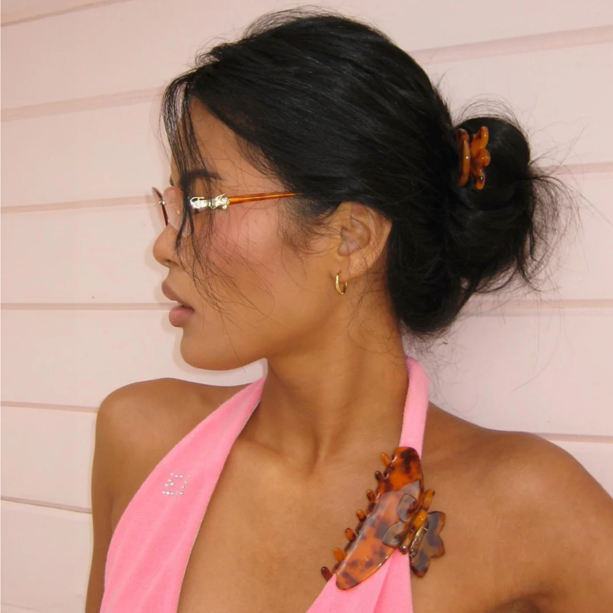 Woman wearing a pink top with decorative hair clip against a light background