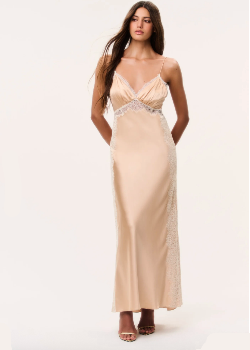 Woman in pale gold silky maxi dress with spaghetti straps on a plain background