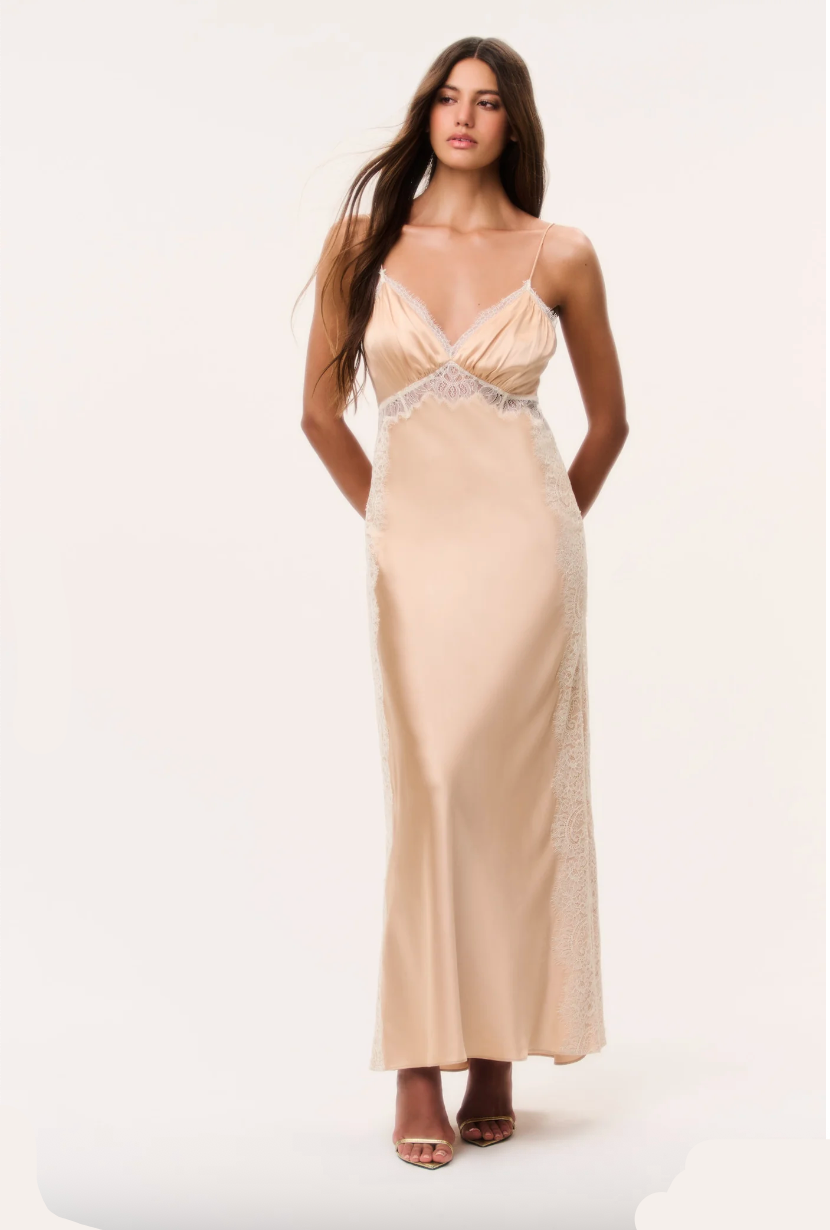 Woman in pale gold silky maxi dress with spaghetti straps on a plain background