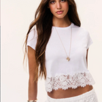 Woman wearing a white cotton tee with a lace trim at the bottom on a plain background