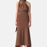 A model wearing a high-neck, halter-style brown dress with a draped side detail and a high-low hemline, paired with black strappy heels, against a light gray studio background.
