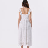 A woman viewed from the back wearing a white lace midi dress with ruffled cap sleeves and a square open back, paired with red high heels, against a plain white studio background.