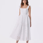 A woman modeling a white eyelet lace midi dress with ruffled shoulder straps, a square neckline, and a flared skirt, photographed against a seamless white studio background.