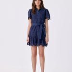 A woman modeling a navy blue lace mini dress with short puff sleeves, a button-up front, and a matching waist tie, photographed against a plain white studio background.