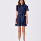 A woman modeling a navy blue lace mini dress with short puff sleeves, a button-up front, and a matching waist tie, photographed against a plain white studio background.