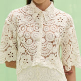Woman wearing a white lace blouse against a light green background
